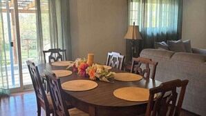 A dining area with a wooden table, chairs, and a floral centerpiece. There is a sofa and a lamp in the background. - Large 4 Bedroom Home - Bryant, AR (Bryant)