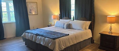A bedroom with a bed, two bedside tables with lamps, a ceiling fan, and a window with curtains.