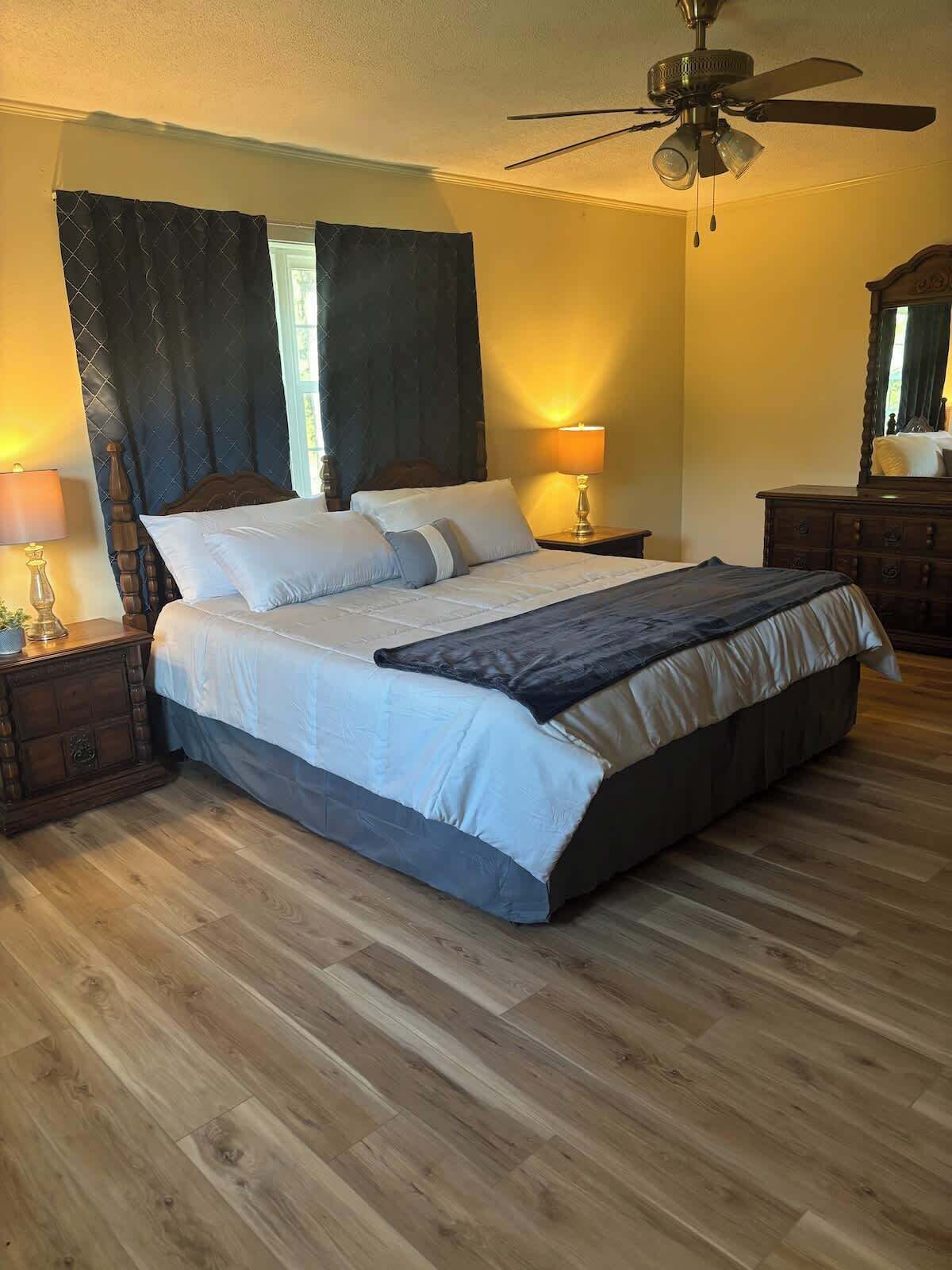 A bedroom with a bed, two bedside tables, a nightstand, a ceiling fan, and a dresser.