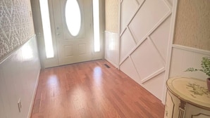 A hallway with wooden flooring, a white door with a window, and a decorative cabinet. - Large 4 Bedroom Home - Bryant, AR (Bryant)