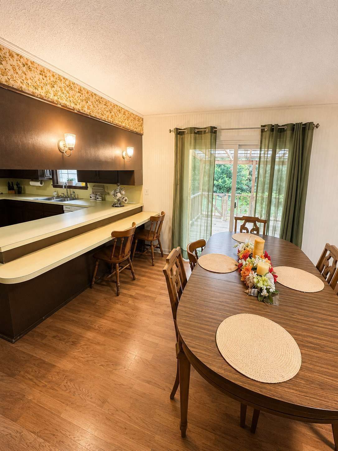A dining area with a wooden table, chairs, and a kitchen with a counter and lights.