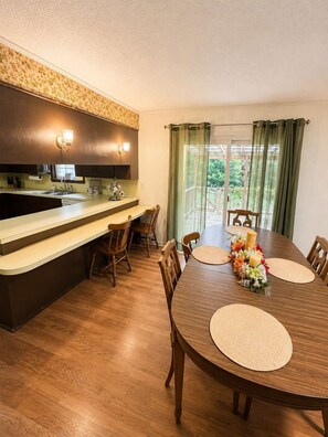 Un comedor con una mesa de madera, sillas y una cocina con mostrador e iluminación.