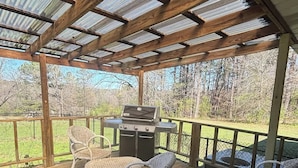 A covered outdoor deck with wicker furniture, a grill, and a view of the surrounding landscape. - Large 4 Bedroom Home - Bryant, AR (Bryant)