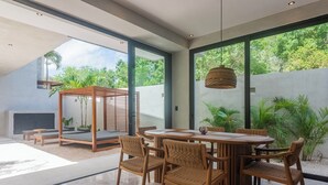 Un espace repas moderne avec une table ronde et six chaises, de grandes fenêtres et des plantes d’intérieur.