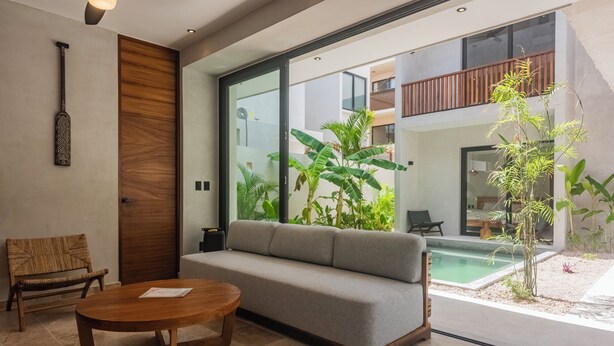 Un salon moderne avec un canapé, une table basse en bois, un fauteuil en osier et une grande porte vitrée donnant sur un espace piscine.