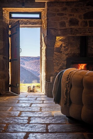 An open doorway leading to a stone interior with a fireplace and a view of a mountainous landscape. - Buron du Tournel, an exceptional gem nestled in an unspoiled mountain setting. (Mandailles-Saint-Julien)
