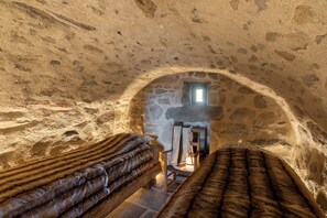 A rustic stone room with two wooden beds, a stone fireplace, and a small window. - Buron du Tournel, an exceptional gem nestled in an unspoiled mountain setting. (Mandailles-Saint-Julien)