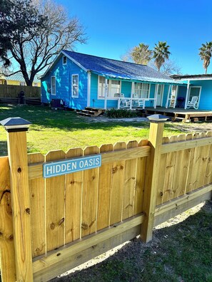 Une maison bleue avec un porche et une clôture en bois sur laquelle est accrochée une pancarte indiquant : « Oasis cachée ».