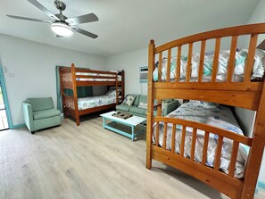 Une chambre avec un lit superposé, un ventilateur de plafond, un canapé vert, une petite table et une fenêtre.