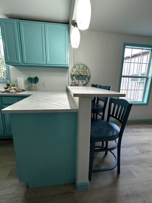A kitchen with teal cabinetry, a marble countertop, and a wall clock. - Hidden Oasis- 2 bdrm 2 bath home (Port O'Connor)
