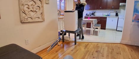 Una sala de estar con un sofá, una mesa de centro y un comedor con mesa y sillas. Se observa una cocina al fondo con gabinetes y electrodomésticos.