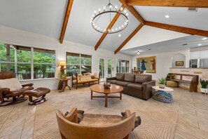 Ein geräumiges Wohnzimmer mit großem Fenster, Holzboden, einer Chandelier und einem Sofa.