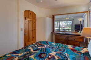 A bedroom with a wooden door, a dresser, a bed with a colorful quilt, a large mirror, a ceiling fan, and a view of the outdoors. - Charming Golf-view Condo With Pool, Hot Tub, Terrace & Wifi (San José del Cabo)