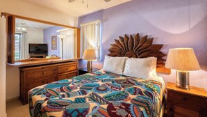 Une chambre à coucher avec un lit, un ventilateur de plafond, une commode, un téléviseur et une fenêtre avec des rideaux.