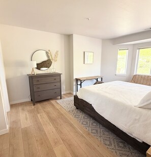 Een slaapkamer met een bed, een kaptafel, een spiegel en ramen.