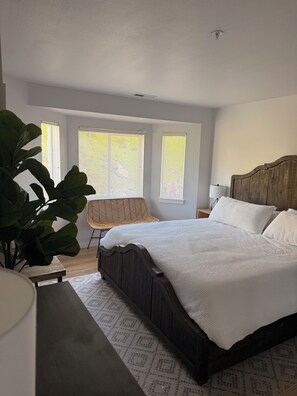 Ein Schlafzimmer mit einem großen Bett, einem Sessel, einem Nachttisch und einer Topfpflanze.