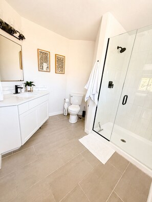 Een moderne badkamer met een douchecabine van glas, witte sanitair en decoratieve muurkunst.