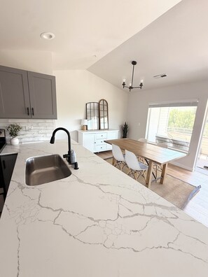 Eine moderne Küche mit Marmorarbeitsplatte, Spüle und einem Essbereich mit Tisch und Stühlen.