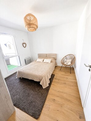 Un dormitorio con cama, una silla, lámpara colgante y ventana.