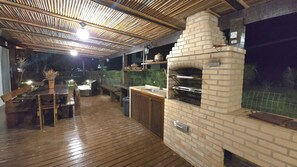 An outdoor patio with a brick oven, wooden furniture, and a bamboo ceiling. - Jardim do Mar - Beachfront Pool, Sports Area, Resort Style (Armação dos Búzios)