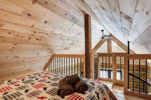 A bedroom with a wooden ceiling, a bed with a quilt, and a window with a view.