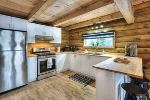 A modern kitchen with stainless steel appliances, wooden cabinetry, and a large island with stools. - Chalet bois rond avec SPA, piscine et petite plage (Mont-Tremblant)