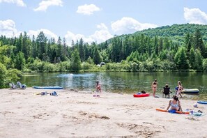 A sandy beach with canoes and kayaks, surrounded by dense forest and a calm river. - Chalet bois rond avec SPA, piscine et petite plage (Mont-Tremblant)