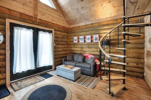 A log cabin interior with a sofa, ottoman, staircase, and framed pictures on the wall. - Chalet bois rond avec SPA, piscine et petite plage (Mont-Tremblant)