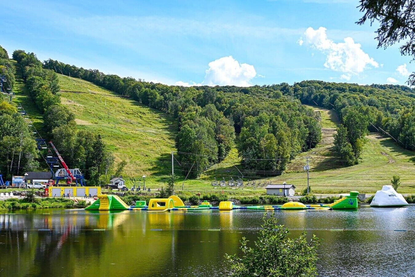 A lakeside view with a water park, a small building, and a hilly landscape.