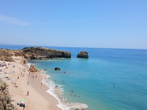 Ein Strand mit klarem Wasser, Felsformationen und Menschen, die das Meer genießen.