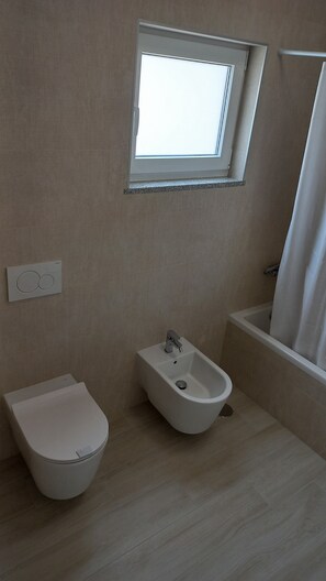 Une salle de bain équipée d’un bidet, de toilettes, d’une fenêtre et d’une baignoire.