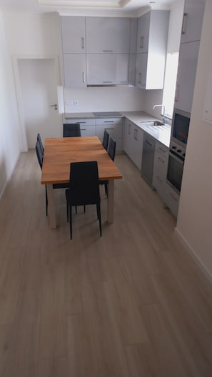 Une cuisine de taille réduite avec des meubles blancs, une table à manger en bois et des chaises noires.