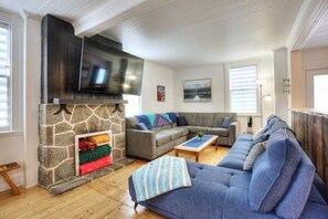 Ein Wohnzimmer mit Kamin aus Stein, einem grauen Sofa, einem blauen Sofa und einem Fernseher, der über dem Kamin angebracht ist.