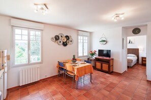 A dining area with a table set for two, a television, and a bed in the background. - La Parenthèse dorée - À moins d’1 km de la plage (Plurien)