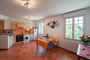 A kitchen with a dining area, a washing machine, a microwave, and a window with a view. - La Parenthèse dorée - À moins d’1 km de la plage (Plurien)