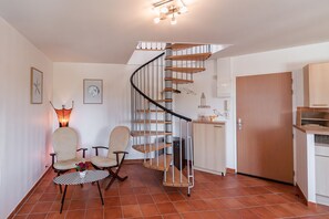 A spiral staircase, two armchairs, a small table with flowers, and a kitchen area. - La Parenthèse dorée - À moins d’1 km de la plage (Plurien)