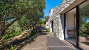 Uma área de estar externa moderna com parede de pedra, deck de madeira e porta de vidro que dá para um cômodo.