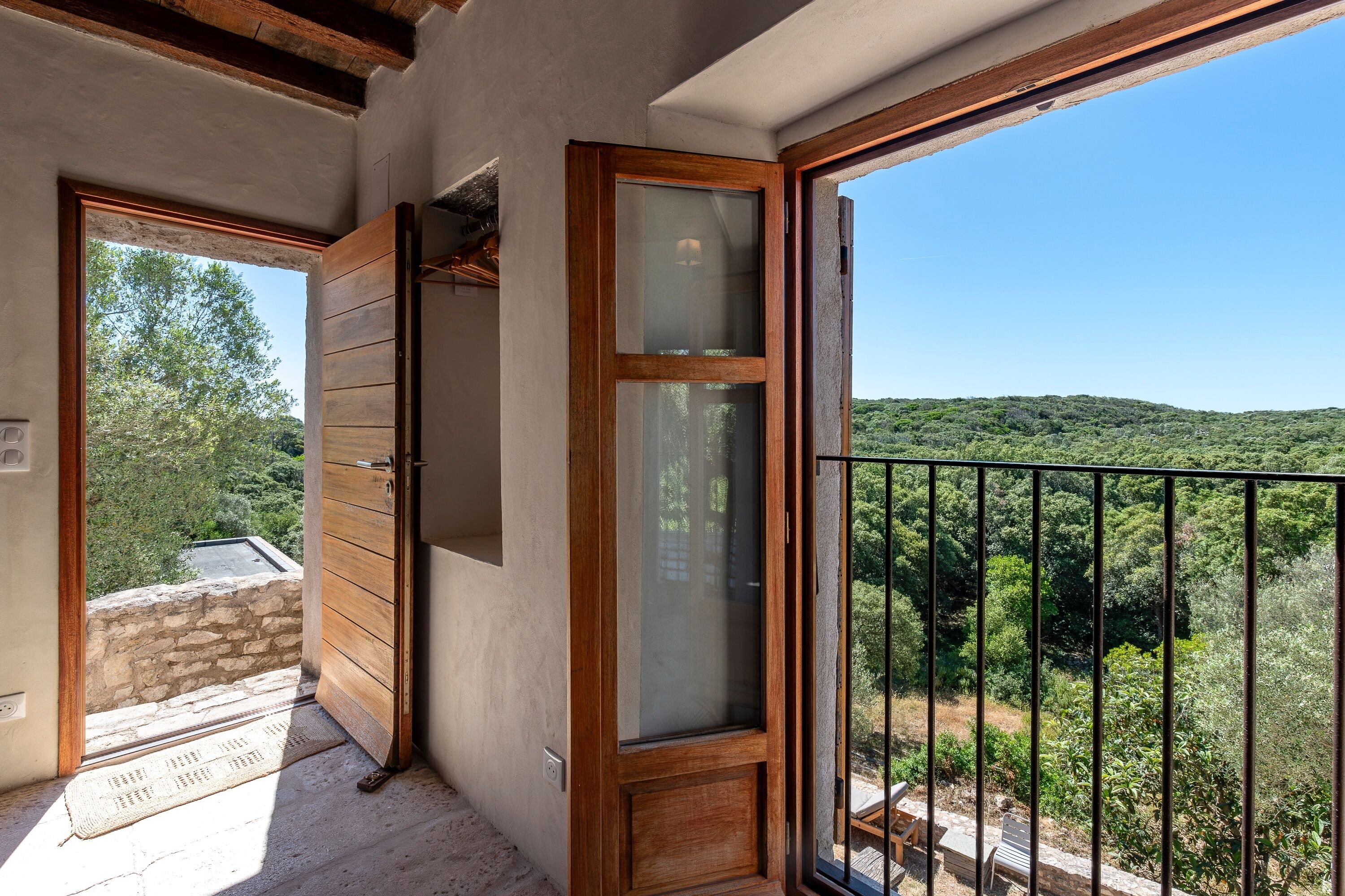 Un balcó amb vista a una vessant boscosa, una porta de fusta i una paret de pedra.