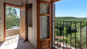 Uma varanda com vista para uma encosta arborizada, uma porta de madeira e um muro de pedra.