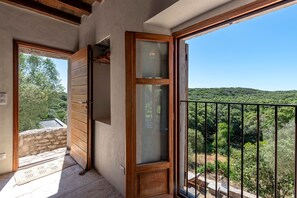 Ein Balkon mit Blick auf einen bewaldeten Hang, eine Holztür und eine Steinmauer.