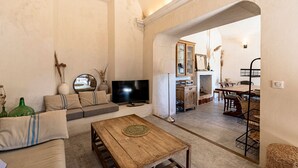 Uma sala de estar com sofá, televisão, mesa de centro de madeira e um espaço de refeições com mesa e cadeiras.
