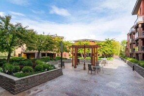Um pátio com pérgola, área de estar e um caminho que leva a um edifício.