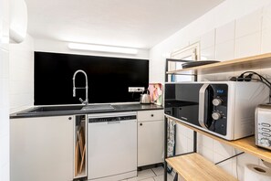 Eine kleine Küche mit Geschirrspüler, Mikrowelle und einer schwarzen Arbeitsplatte.