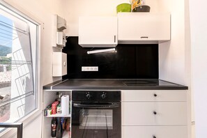 A compact kitchen with a built-in oven, a small shelf with kitchen items, and a window with a view of the outside. - Casa Soprana - À moins d'1 km de la plage (L'Île-Rousse)