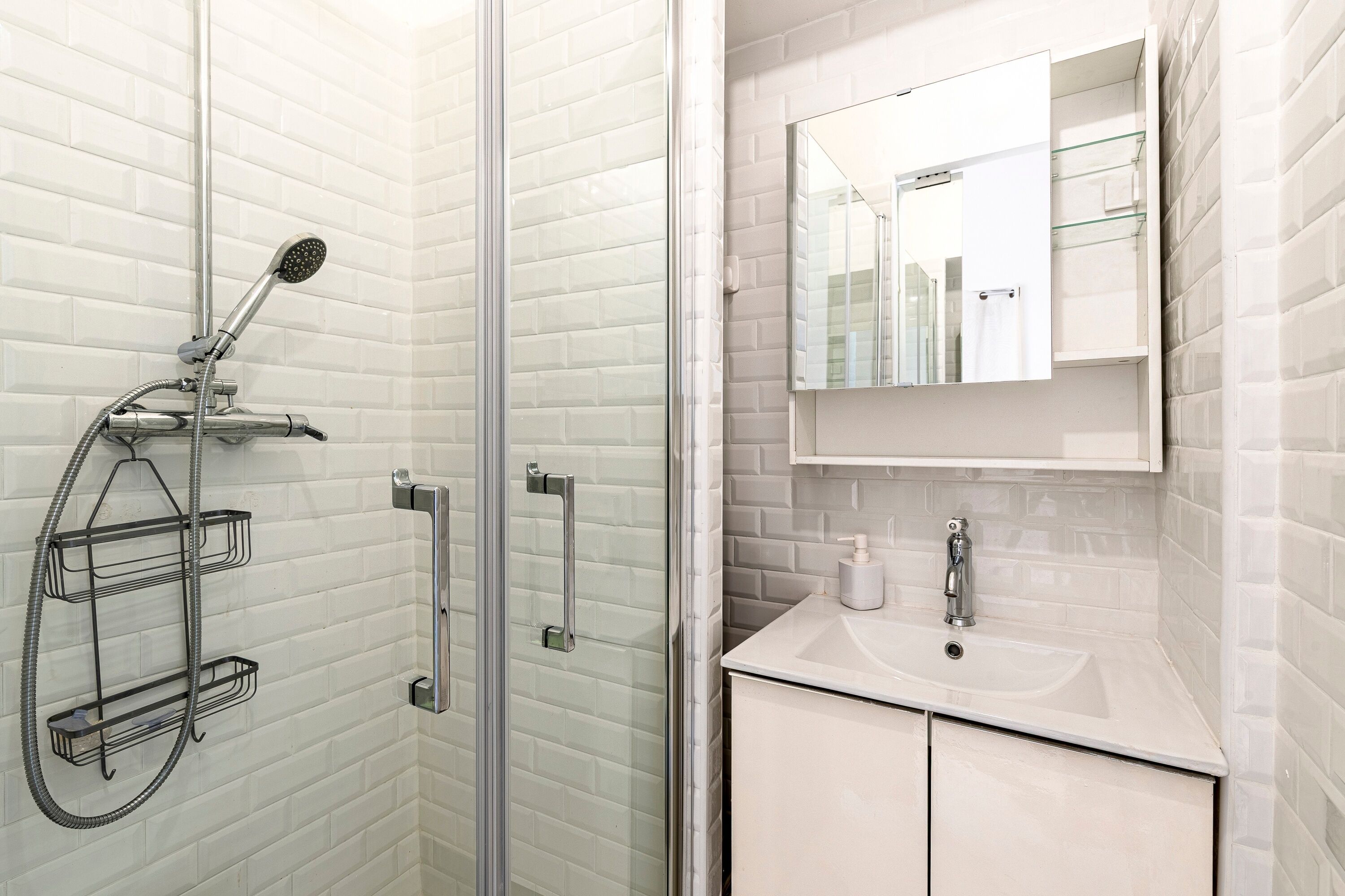 A bathroom with a glass shower enclosure, a white sink, a mirror, and a towel rack.