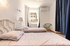 Ein Schlafzimmer mit Bett, Stuhl, Lampe und Fenster mit Blick auf Gebäude.