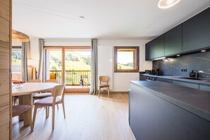 Eine moderne Küche mit dunklen Schränken, einem Holzesstisch und Stühlen. Ein Fenster bietet Blick auf eine grüne Landschaft.
