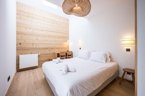 Ein Schlafzimmer mit einer Holzwand, einem Bett mit weißer Bettwäsche, einem kleinen Tisch und einer Pendelleuchte.