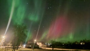 Escena nocturna con auroras boreales, farolas y un edificio al fondo.