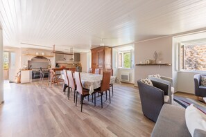 A spacious living area with a dining table, chairs, a sofa, and a kitchen in the background. - Maison Paulette - Belle maison pour 8 en altitude (Neussargues en Pinatelle)